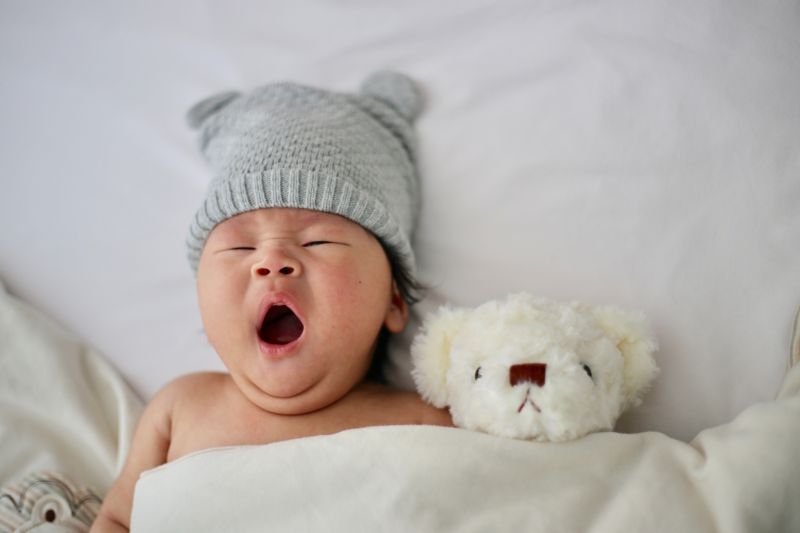 A yawning baby with a teddy bear
