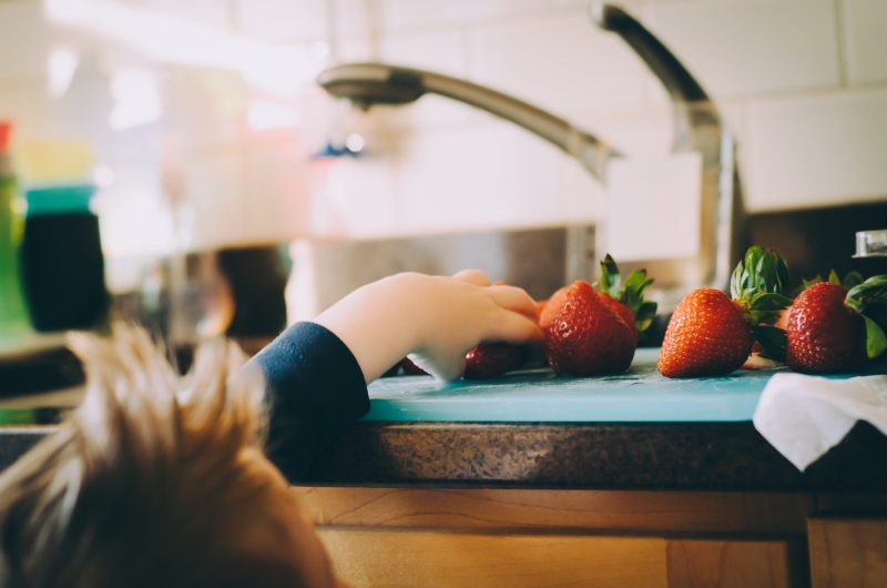 A child reaches for some strawberries on a counter top